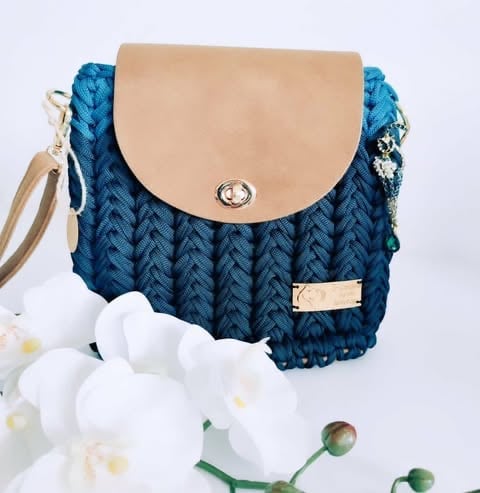 Blue quilted shoulder bag with beige leather flap and metal clasp, displayed with white flowers