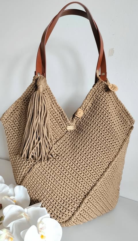 Beige woven tote bag with brown leather handles and fringe tassel detail, displayed against white background
