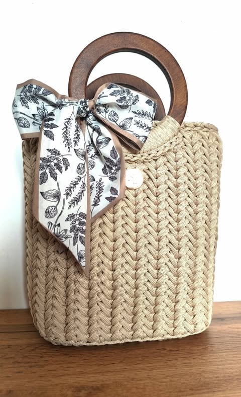Beige woven tote bag with wooden handles and a botanical print fabric scarf tied to one handle