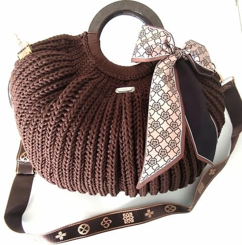 Brown knitted shoulder bag with decorative bow, metal handles, and patterned shoulder strap