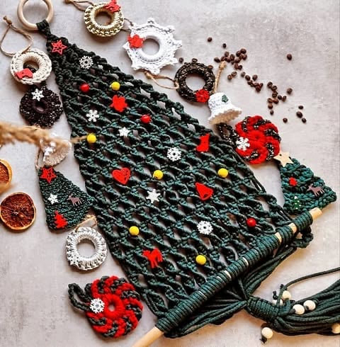 Decorative crochet Christmas tree with colorful ornaments and beads surrounded by festive holiday decorations on a light surface