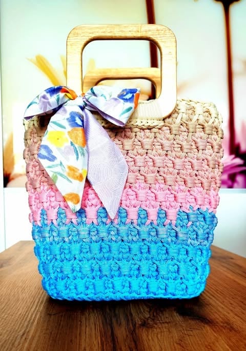 Colorful woven basket with wooden handles and rainbow striped pattern in pink, blue, and tan, decorated with a floral ribbon bow
